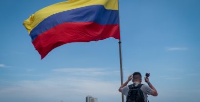 Un hombre ondeando una bandera colombiana frente a una ciudad.
