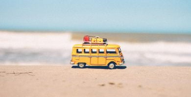 Un autobús de juguete amarillo se encuentra en la playa junto al océano.